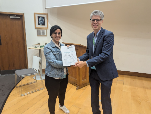 A photo of a man and woman smiling for the camera as the man on the right gives a certificate to the woman on the left