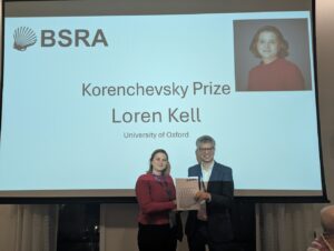 Two people shaking hands, as one receives the Korenchevsky Prize